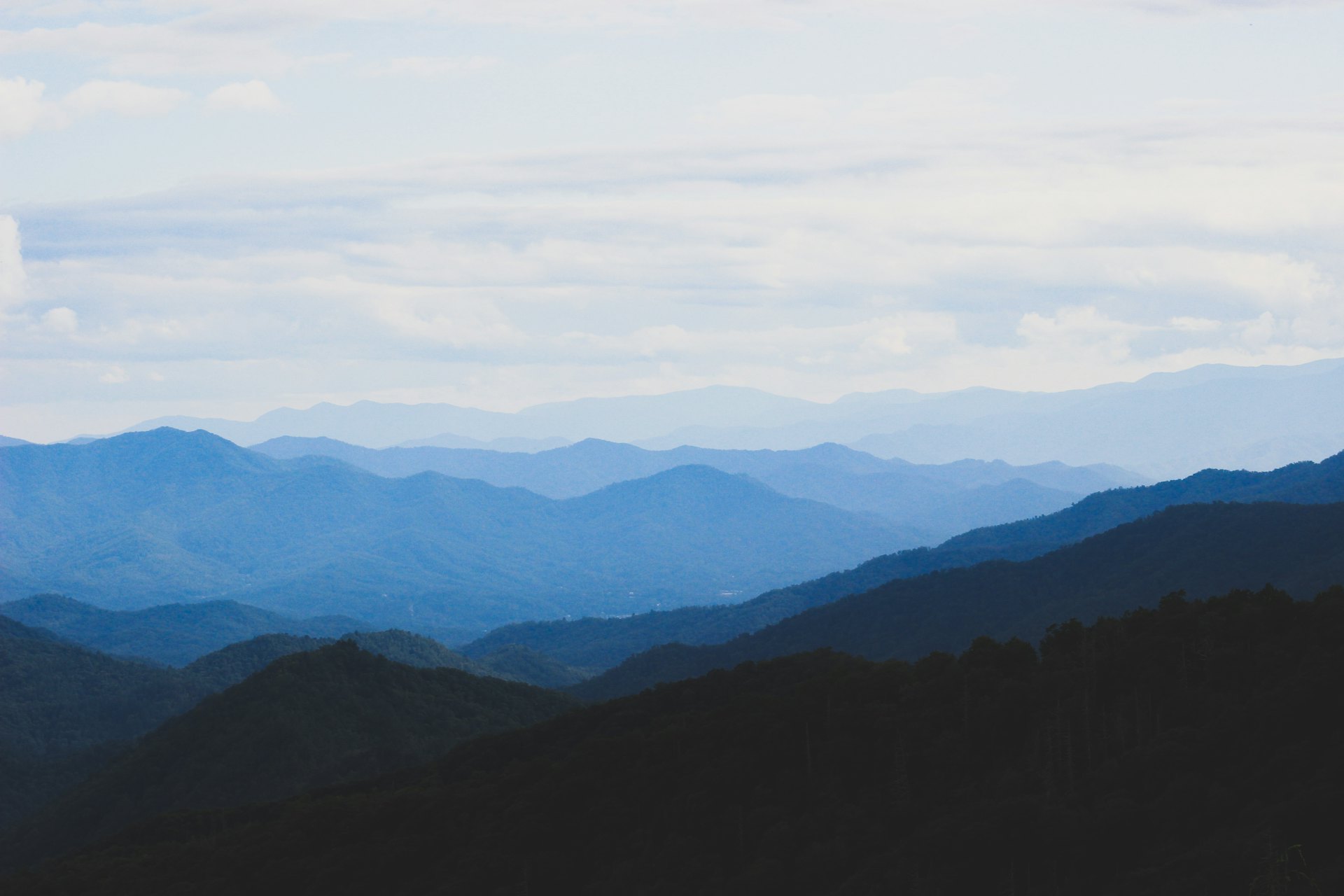Calm, layered blue mountains under a soft clouded sky